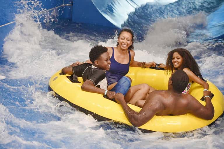 Family of four enjoying a yellow inflatable raft ride in a wave pool attraction