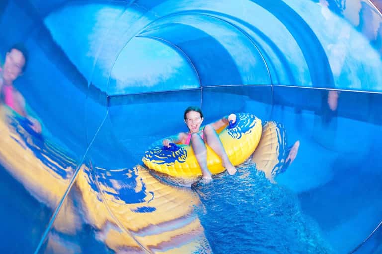 Child on yellow inflatable raft going through blue water slide tunnel
