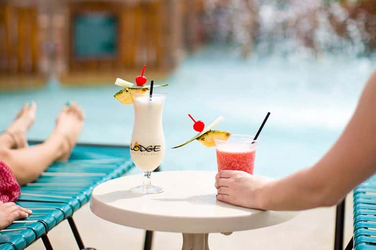 Tropical cocktails on poolside table with resort guests relaxing on lounge chairs in background