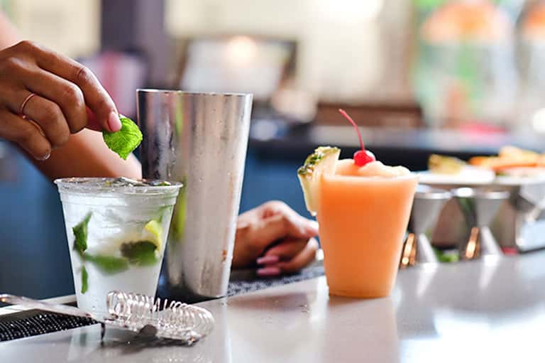 Bartender preparing cocktails with fresh mint and citrus garnishes at a resort bar