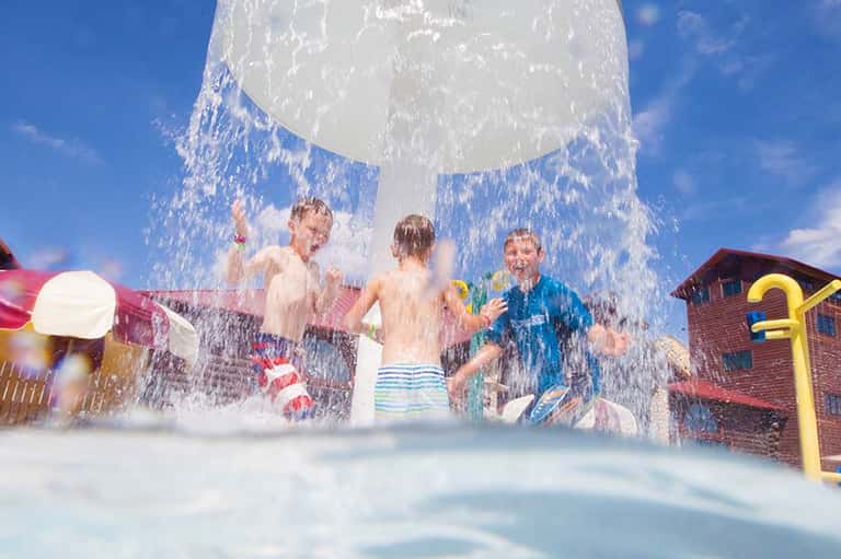 Children playing under a large bucket-shaped water dumper at a water park splash area