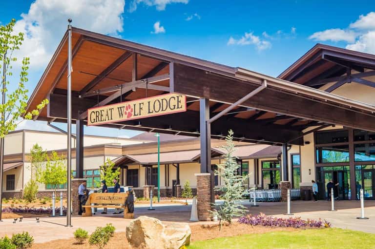 Great Wolf Lodge exterior with wooden architecture, covered pavilion entrance, and landscaped grounds under blue sky