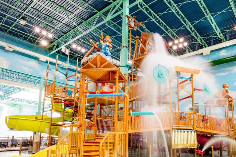 Indoor water park with colorful wooden play structure, water slides, and splash features