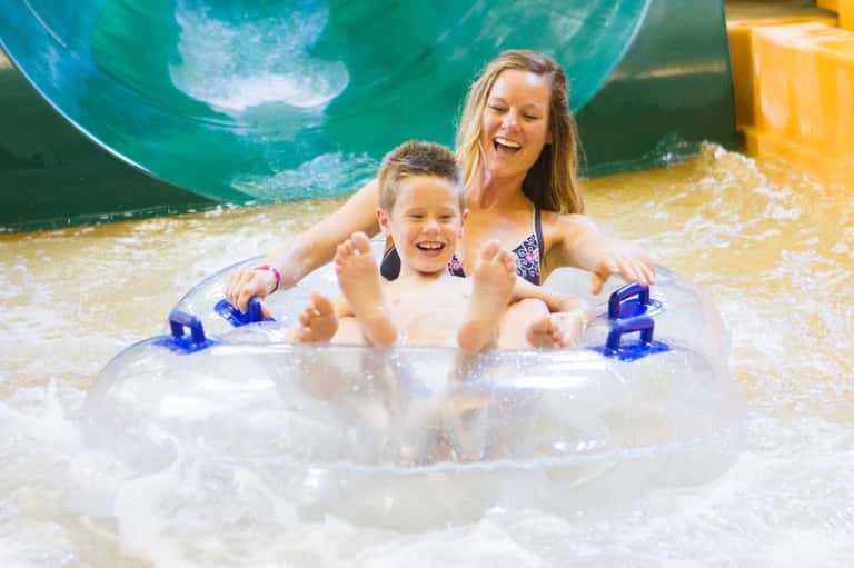 Woman and child on inflatable raft in shallow wave pool with water slides