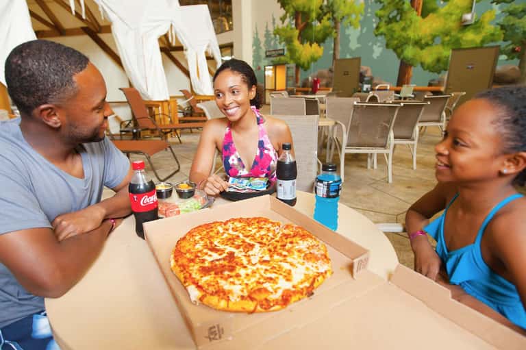 Group of three people enjoying pizza and beverages in casual outdoor dining area