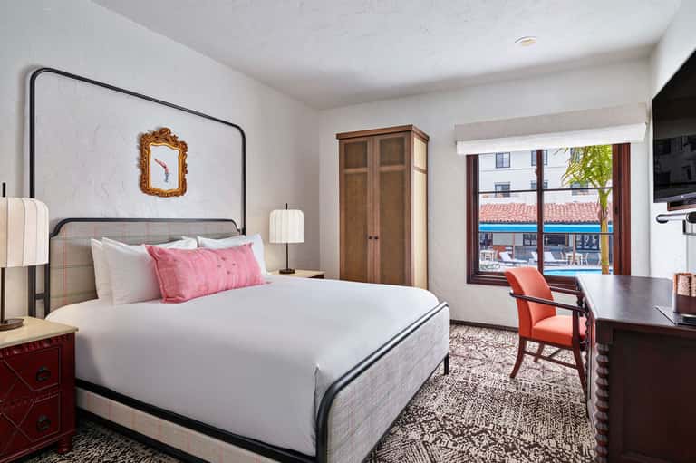 Modern hotel bedroom with white bedding, pink pillows, metal frame bed, and ocean view