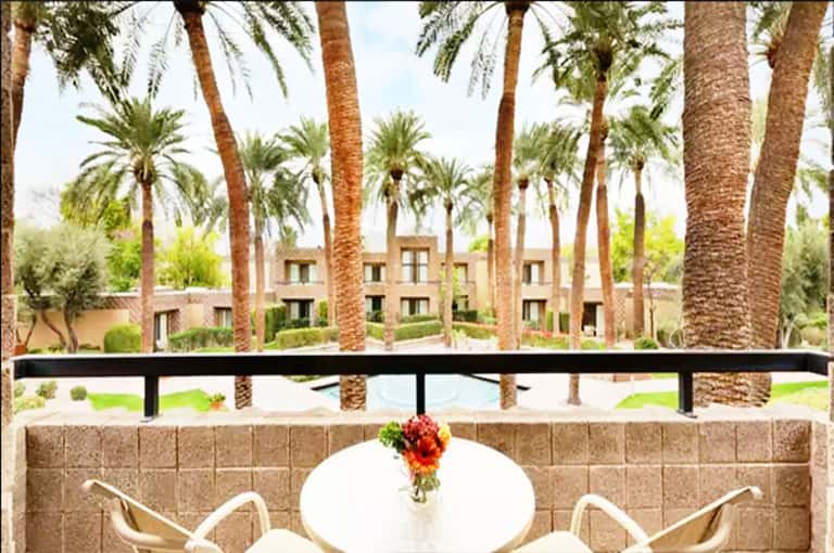 Balcony terrace with white chairs overlooking palm trees and resort courtyard with water feature