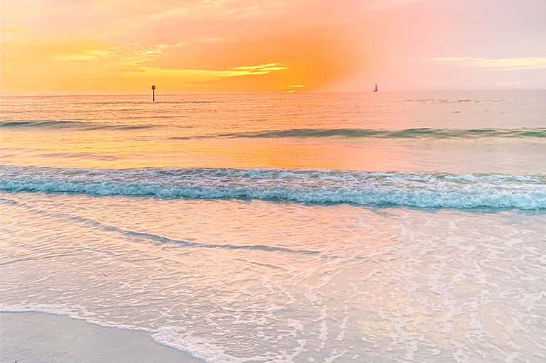 Golden sunset over calm ocean waves with blue water and sandy shore