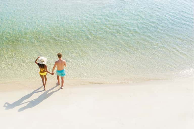 Aerial view of two children holding hands entering clear turquoise ocean water on a beach