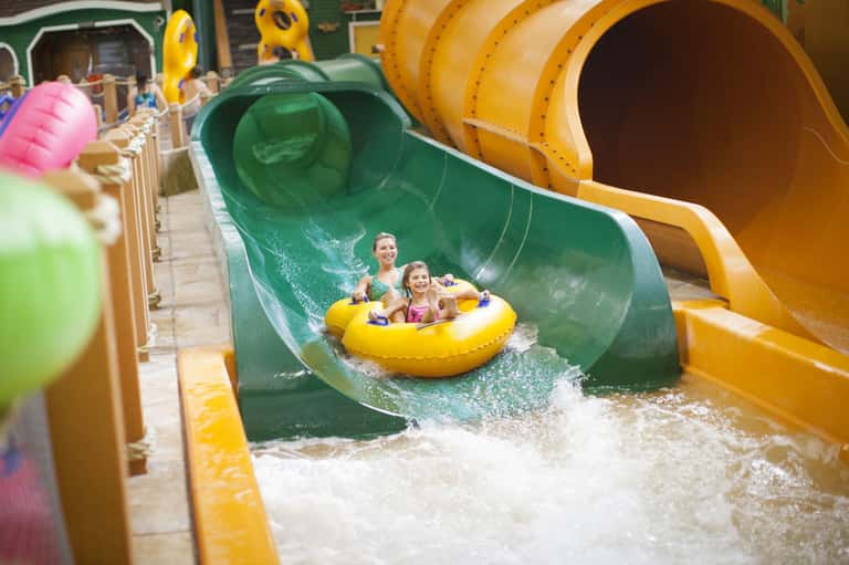 Family riding yellow raft down green water slide at an indoor water park attraction