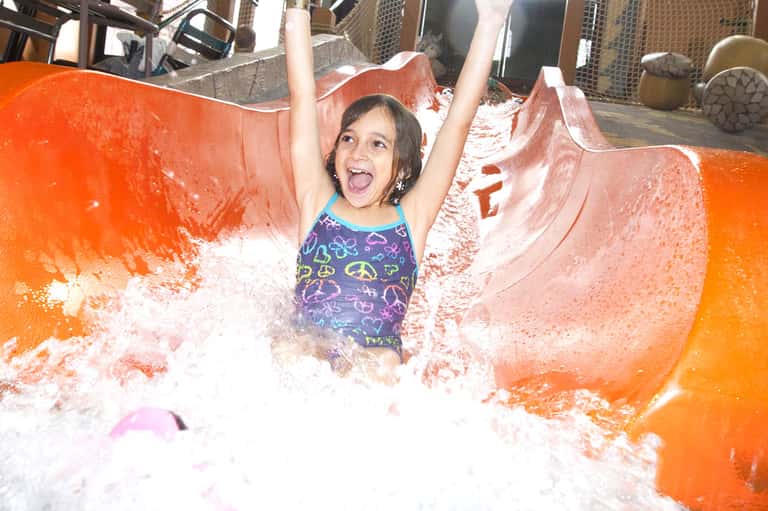 Young girl splashing in a foam water slide with orange sides at an indoor water park