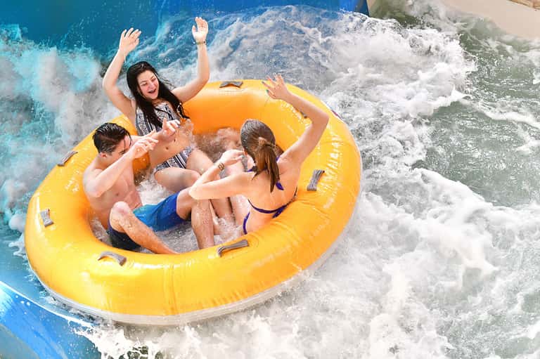 Group of people riding a yellow inflatable tube through ocean waves at a water park