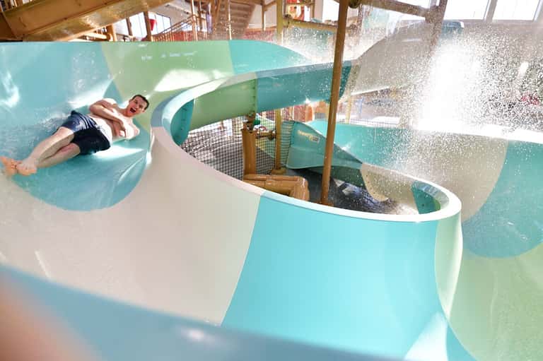 Man sliding down turquoise water slide at indoor water park facility