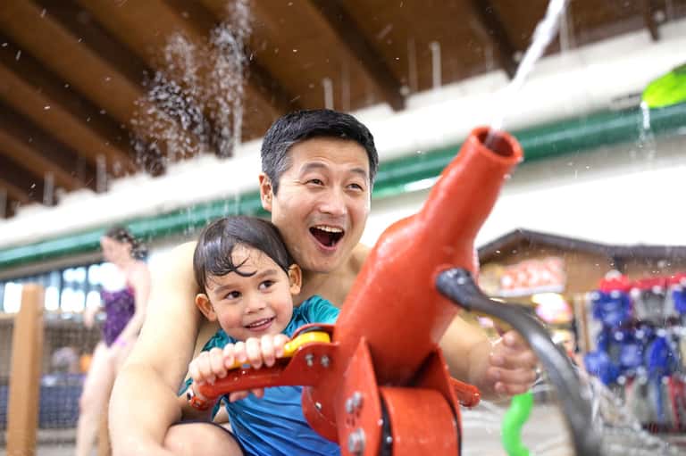 Father and child playing with red toy at indoor water park facility