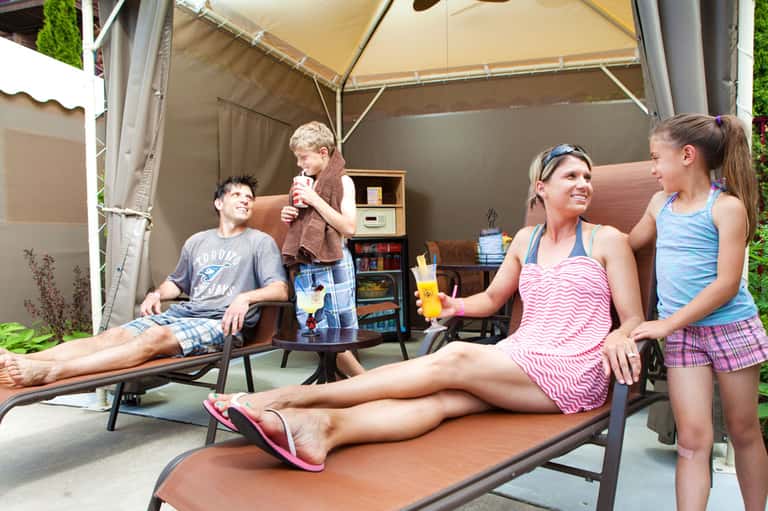 Family relaxing under a tan cabana tent with lounge chairs and beverages