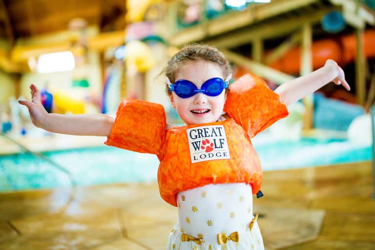 Young child wearing orange shirt and blue goggles at indoor water park with inflatable arm floaties
