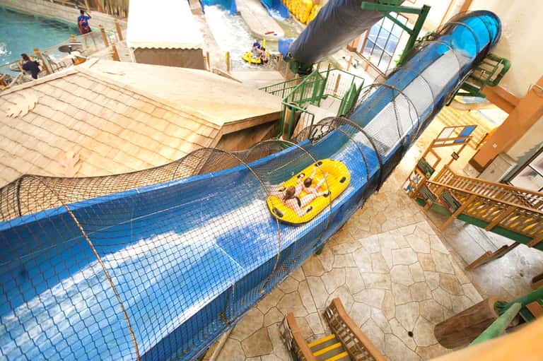 Blue water slide tunnel at indoor water park with yellow raft descending through curved mesh enclosure