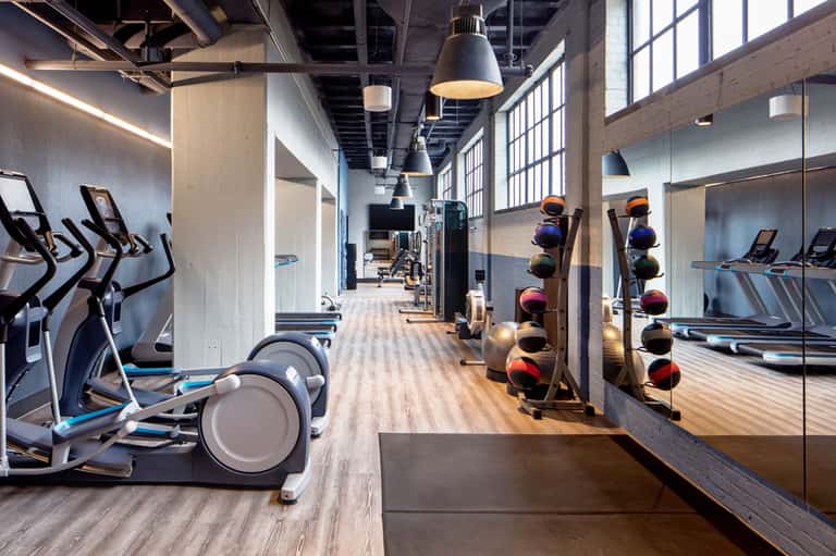 Modern gym interior with cardio equipment, dumbbells, mirrors, and industrial ceiling design