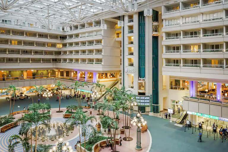Modern hotel atrium with multiple floors, indoor gardens, and ambient lighting