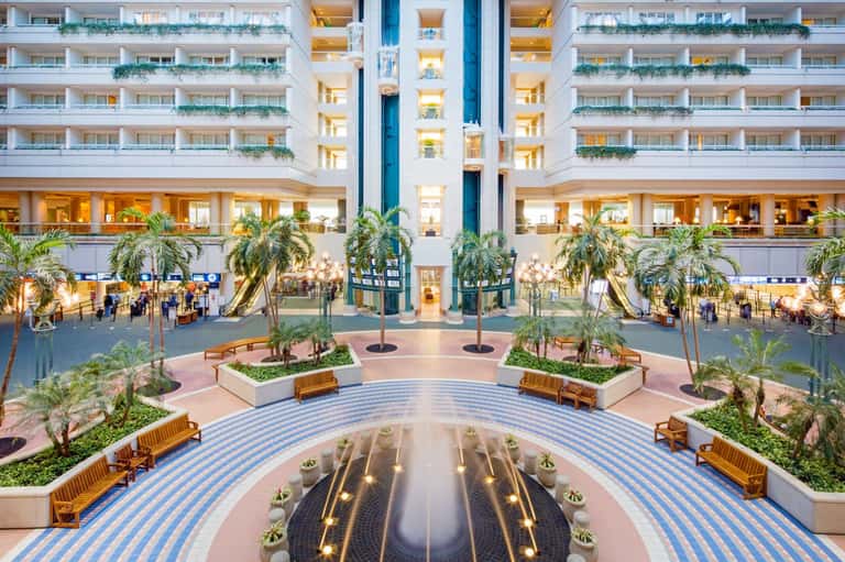 Modern hotel atrium with central fountain, palm trees, and multi-story balconies