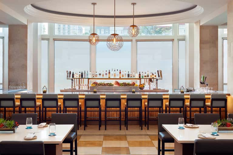 Modern bar with pendant lights, extensive liquor selection, and panoramic city views through floor-to-ceiling windows