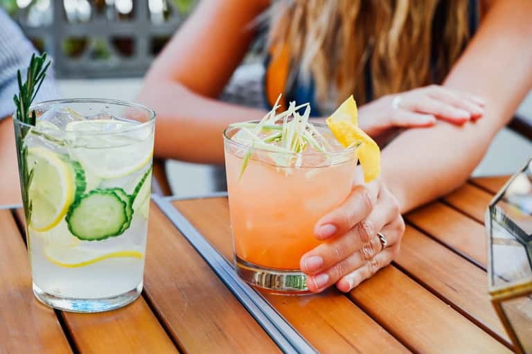 Two refreshing cocktails with fresh fruit garnishes on wooden poolside table