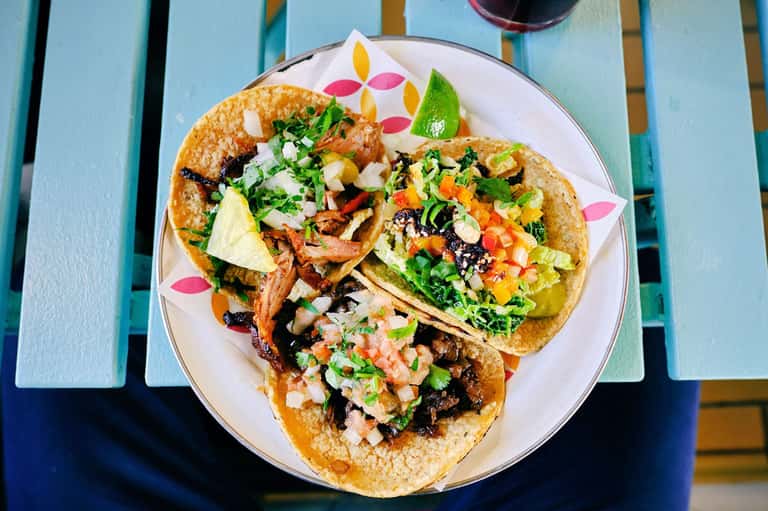 Three gourmet tacos on white plate with colorful garnishes