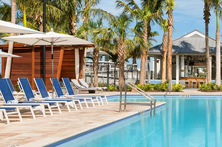 Resort pool with blue lounge chairs, white umbrellas, and palm trees surrounding the deck area