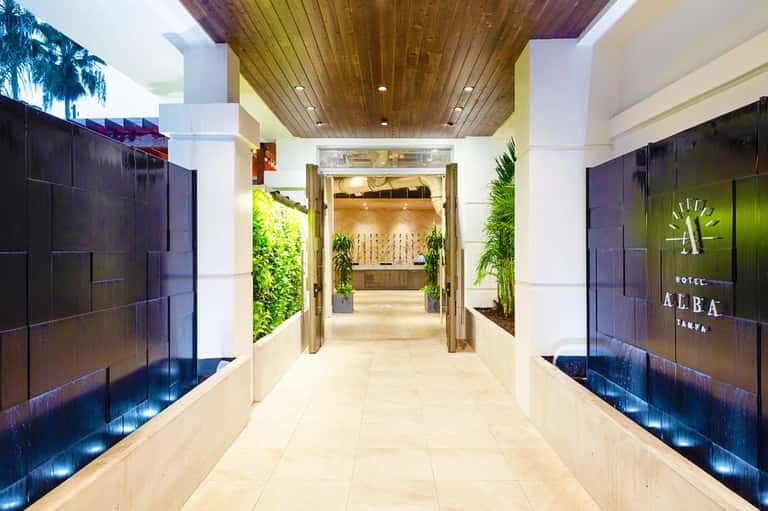 Modern hotel corridor with green living walls, wooden ceiling, and dark glass entrance doors leading to reception area