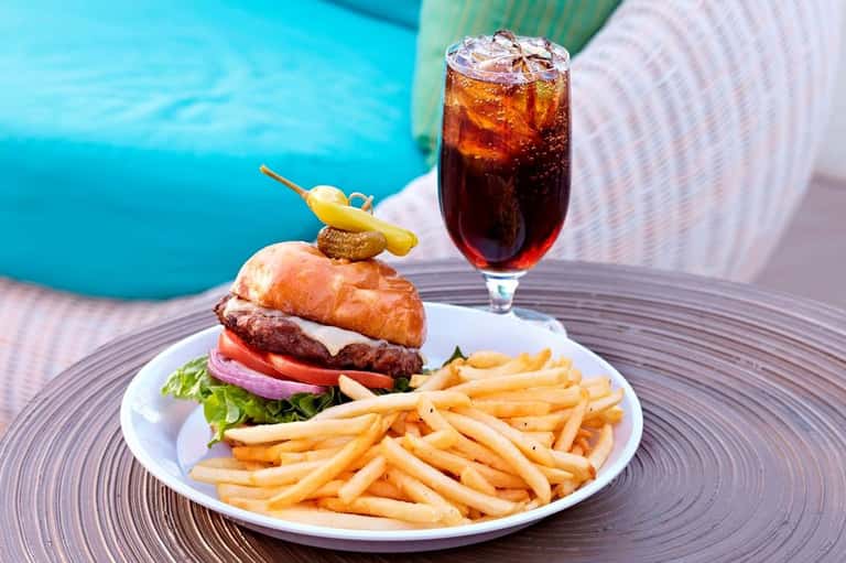 Burger with fries and a cola drink by a pool at a resort