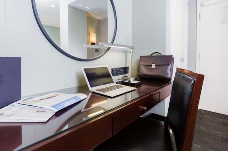 Modern hotel business center with desk, laptop, briefcase, round mirror, and professional furnishings