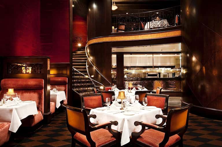 Upscale fine dining restaurant with burgundy velvet seating, open kitchen, and modern spiral staircase