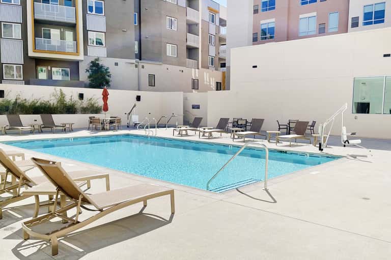 Resort swimming pool surrounded by lounge chairs and modern apartment buildings
