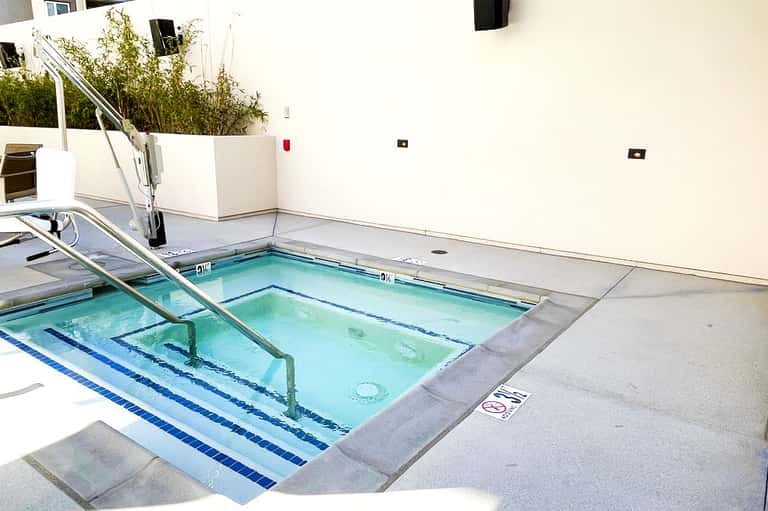 Outdoor lap pool with blue water and lane markers, surrounded by concrete deck and white building walls