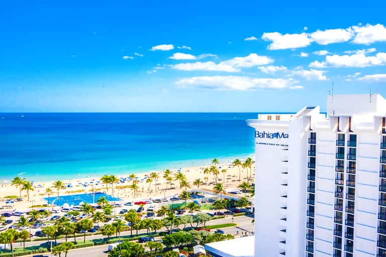 Bahia Mar beachfront hotel with white facade overlooking sandy beach, palm trees, and turquoise ocean