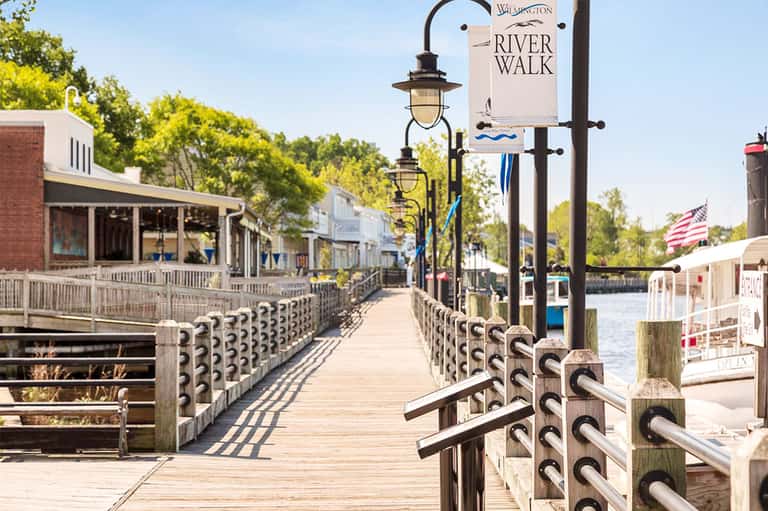 Waterfront boardwalk with shops and lamp posts along the river