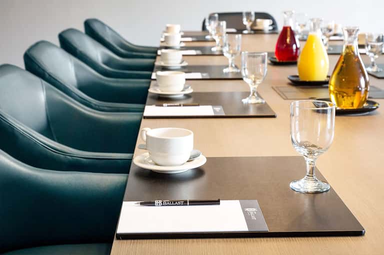 Conference room table set with place settings, coffee cups, water glasses, and condiments for meeting