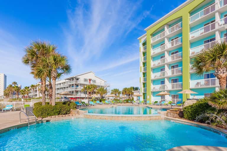 Resort pool with tropical palm trees and colorful multi-story hotel building against blue sky