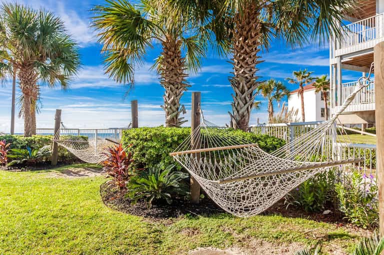 Oceanfront lawn with white hammocks strung between palm trees and beach access