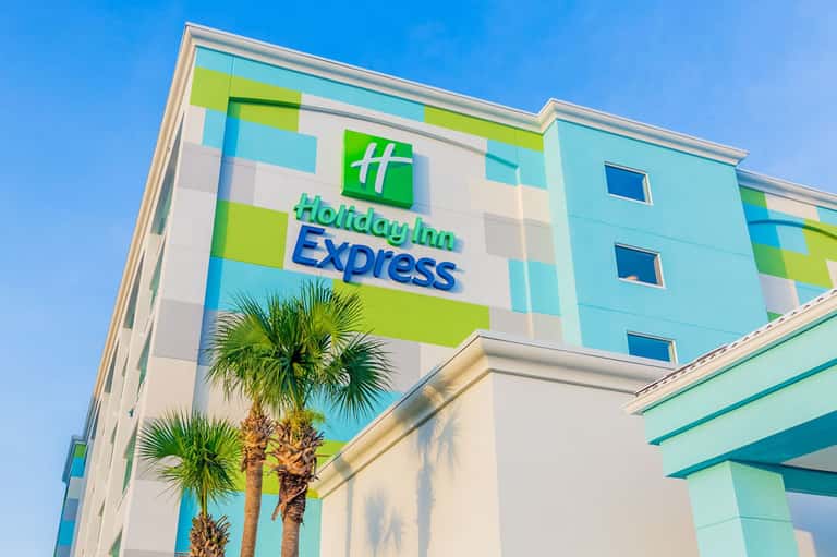 Holiday Inn Express hotel exterior with colorful geometric design and palm trees under clear blue sky