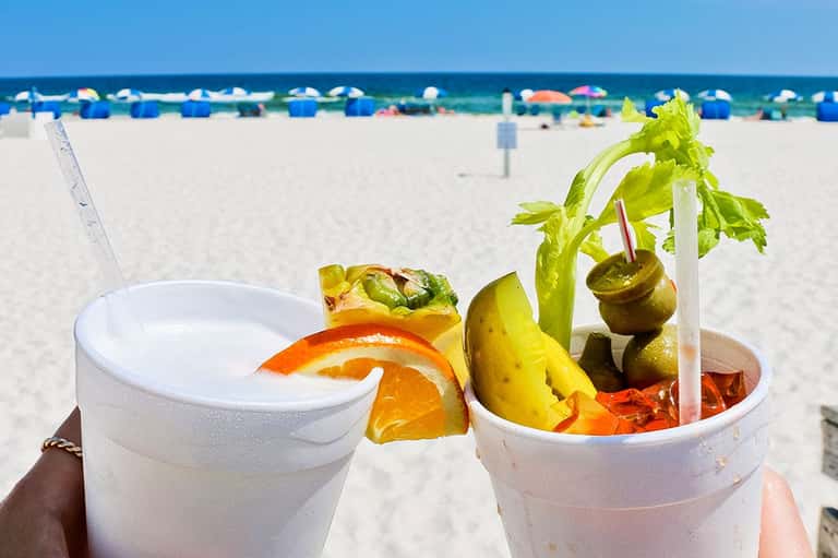 Beach cocktails with fresh fruit and orange slice on sandy shore with blue umbrellas