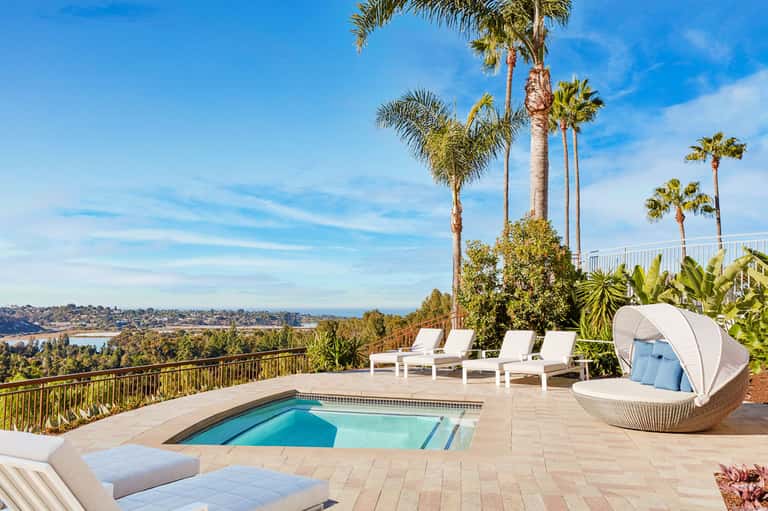 Luxury hilltop pool deck with white lounge chairs, palm trees, and panoramic bay views