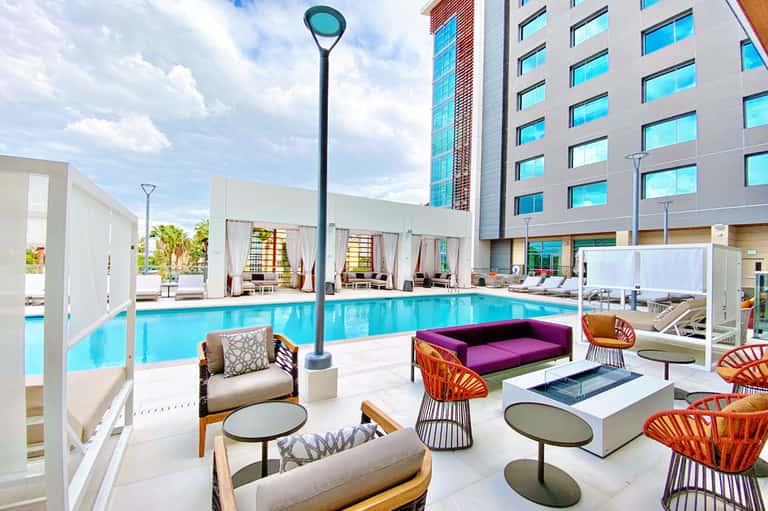 Modern resort pool deck with lounge chairs, colorful seating, and high-rise hotel building