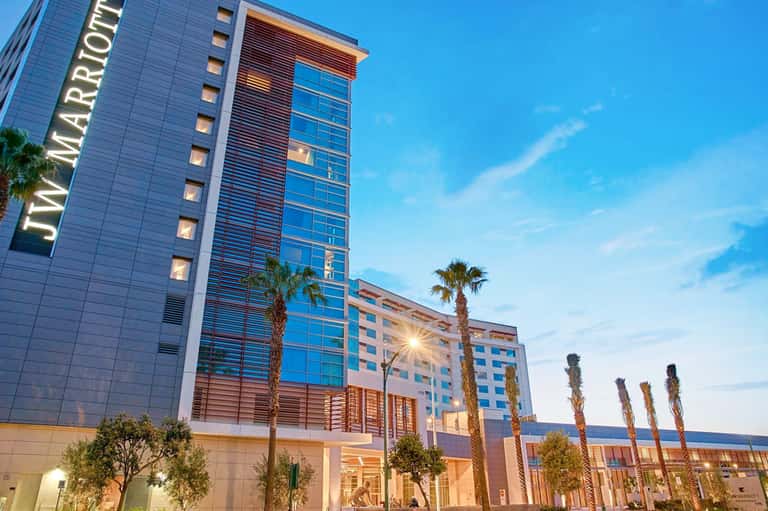 Modern hotel exterior at dusk with glass tower, palm trees, and lit entrance