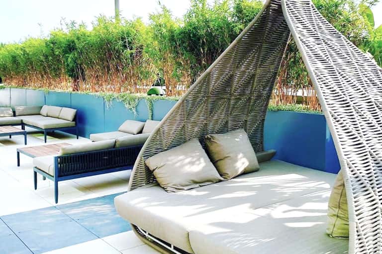 Outdoor lounge area with woven daybed canopy, blue accent wall, and lush green bamboo privacy screening