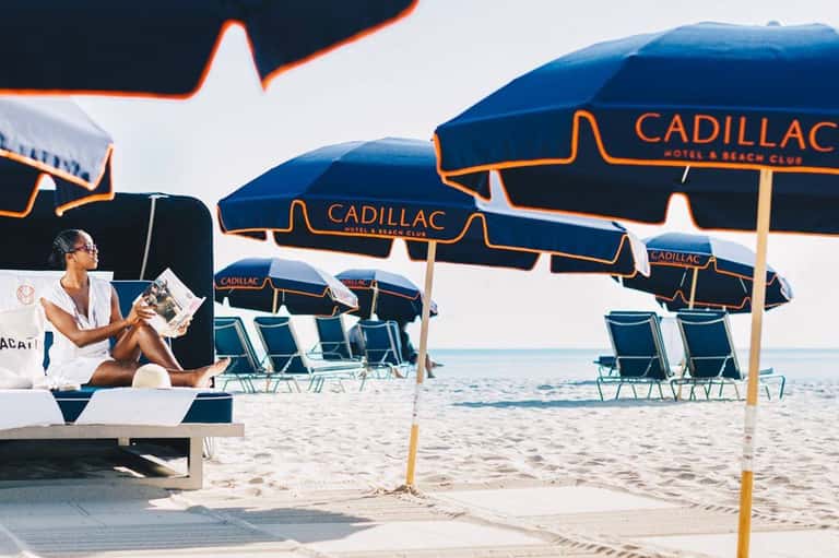 Woman relaxing on beach under branded Cadillac umbrellas with beach chairs and ocean