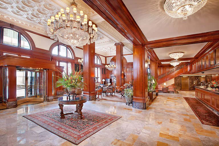 Luxurious hotel lobby with ornate wooden columns, crystal chandeliers, and marble floors