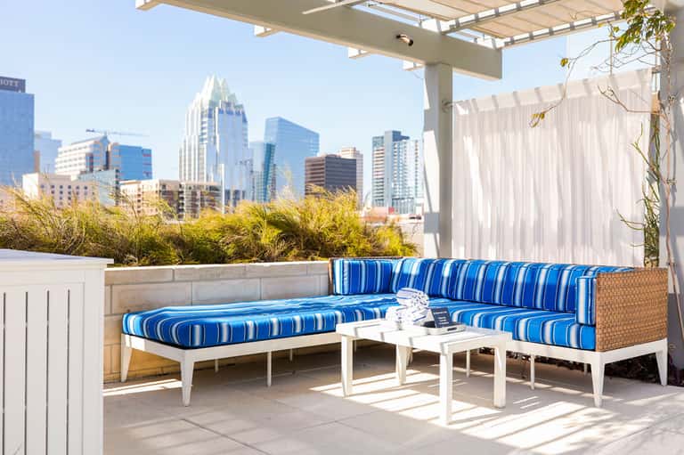 Urban rooftop lounge with blue striped seating, city skyline views, and modern pergola shade structure