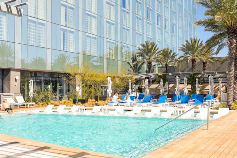 Resort pool with turquoise water, white lounge chairs, and modern high-rise building