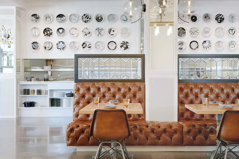 Modern dining area with tufted cognac leather banquette, decorative plate wall display, and geometric glass-fronted cabinetry.